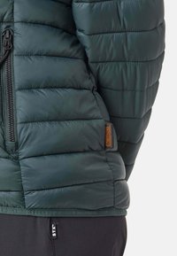 Grüne Steppjacke mit genähter Textur, ausgestattet mit einem Reißverschluss vorne und einem orangefarbenen Logoetikett. Gummizug am Saum und an den Bündchen für einen taillierten Schnitt.