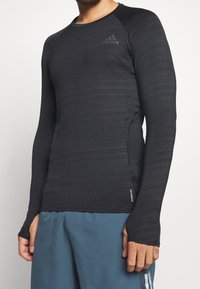 Czarny sportowy t-shirt z długim rękawem w teksturowanej tkaninie. Posiada okrągły dekolt i logo na klatce piersiowej. Szycie po bokach z metką "AEROREADY".