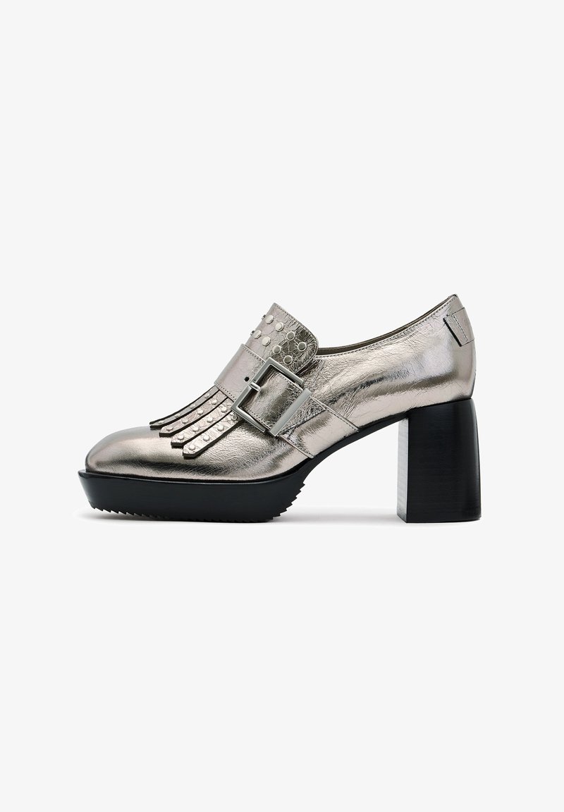 Mocassin en cuir argenté métallique avec franges et clous, large bride à boucle, semelle noire épaisse et talon carré.