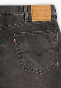 Grå denimjeans med en läderetikett med "Levi Strauss & Co." vid midjan. Bakfickan har signaturens böjda söm.