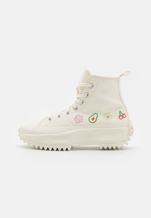 Crèmekleurige hoge canvas sneaker met dikke geribbelde zool, veters aan de voorkant en geborduurde avocado, kersen en bloemen aan de zijkant.