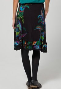 Czarna spódnica z kolorowymi wzorami kwiatów i pawich piór, z falbaniastym dołem i lekkim, zwiewnym materiałem. Noszona z czarnymi rajstopami.
