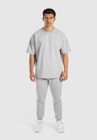T-shirt en coton gris à manches courtes, associée à un pantalon de survêtement en coton gris. Les deux ont une coupe décontractée et des détails de design minimalistes.