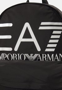 Zaino nero realizzato in materiale resistente, con grandi loghi bianchi, motivi geometrici e dettagli testurizzati nella parte inferiore.