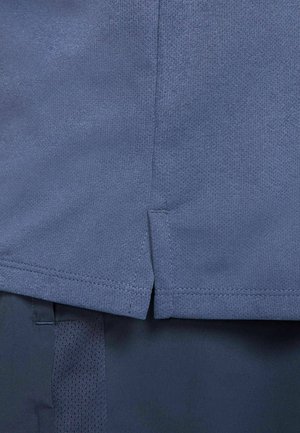 Camisa deportiva azul con un tejido texturizado y transpirable. Presenta una ligera abertura en el dobladillo y costuras cosidas a lo largo de los bordes.
