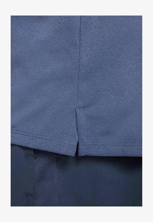 Blauwe sportshirt van een textuur, ademend materiaal. Heeft een lichte split aan de onderrand en gestikte naden langs de randen.