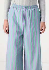 Lightweight, purple and green vertically striped wide-leg pants with an elastic waistband and drawstring detail. Smooth cotton fabric.