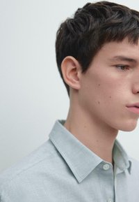 Camicia a maniche corte azzurro chiaro con colletto classico. Il tessuto appare liscio e leggermente strutturato. Il volto del modello è parzialmente visibile.