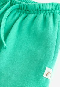 Pantalons de jogging en coton turquoise avec une taille élastique et un cordon de serrage. Présente une étiquette avec un design de rainbow simple. Texture douce.