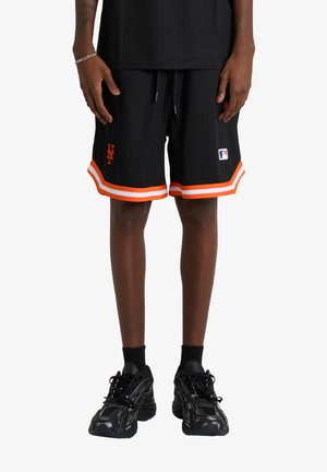 Persona vistiendo pantalones cortos de baloncesto negros de New York Mets con ribete naranja y blanco, zapatillas negras y calcetines negros, de pie con las manos relajadas.