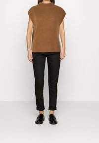 Bruine gebreide top met een hoge hals en korte mouwen, gecombineerd met zwarte slim-fit pantalon en glanzende zwarte loafers. Eenvoudig ontwerp.