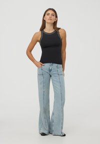 Czarny top bez rękawów o dopasowanym fasonie z metalicznymi akcentami przy dekolcie, zestawiony z jasnoniebieskimi dżinsami w kształcie dzwonów z pionowymi szwami.