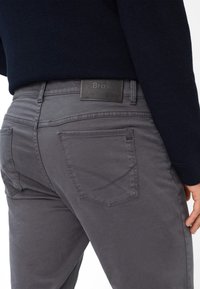 Pantaloni in denim grigio con design aderente, caratterizzati da una cintura nera a trama, tasche posteriori con dettagli a punto croce e una texture liscia.