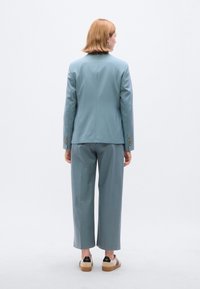 Ανοιχτό μπλε σακάκι κοστουμιού ραμμένο με ευθεία σχεδίαση, συνδυασμένο με παντελόνια φαρδύ καβάλο. Διακοσμημένο με χρυσά κουμπιά και επίπεδα παπούτσια.