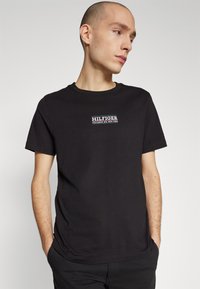Maglietta a maniche corte in cotone nero con scollo rotondo, caratterizzata da un logo ricamato bianco sul petto con la scritta "HILFIGER COLUMBUS AVE. NEW YORK."
