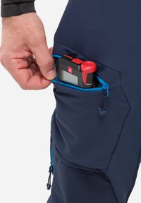 Un pantalon bleu marine en tissu texturé comporte une poche latérale, tenant en toute sécurité un dispositif de mesure noir et rouge, mis en valeur par des zips bleus.