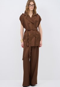 Bruin op maat gemaakte twee-delige outfit met een wikkelstijl top met schouderknopen, wijde broekspijpen en een bijpassende riem. Glad textuur.