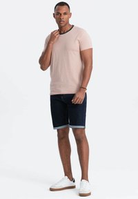 Lyserød t-shirt med sort halsudskæring, parret med mørke denimshorts og hvide sneakers med brune detaljer. En enkel, afslappet påklædning.