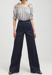 Marintröjor med vida ben i kombination med en vit och svart randig off-shoulder top. Toppen har knytband och är tillverkad i ett lätt material.