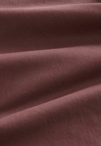 Tela de algodón en un tono burdeos profundo, con una textura suave y un ligero brillo, presentando pliegues diagonales que crean suaves arrugas y sombras.