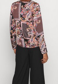 Langärmlige Bluse mit schwarzem Grund und kunstvollen mehrfarbigen Paisley- und geometrischen Mustern. Weicher Stoff mit tailliertem Design.