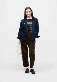 Veste bleu foncé avec boutons dorés, haut rayé noir et blanc, pantalon en velours côtelé marron et chaussures noires. Sac à main blanc en accessoire.
