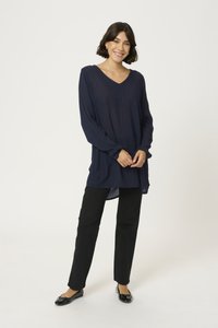 Tunic blu navy a maniche lunghe con scollo a V, in tessuto leggero e con spacchi laterali, abbinata a pantaloni neri a gamba dritta e scarpe nere basse.
