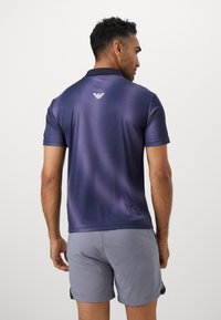 Kortermet polo skjorte i mørk lilla, med teksturert stoff, flat krage og liten logo bak. Kombinert med lysegrå shorts.