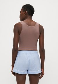 Bruine katoenen tanktop gecombineerd met lichtblauwe gestreepte shorts met een opgelegd zoom en een elastische tailleband, gezien vanuit de achterkant.