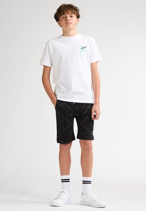 Camiseta blanca, pantalones cortos negros con patrones geométricos y zapatillas blancas. Calcetines con dos rayas negras cerca de la parte superior. Talla juvenil.