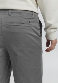 Pantalones de algodón grises con una textura suave, que cuentan con un bolsillo trasero, pasadores para cinturón y un diseño de pierna ligeramente ajustada.