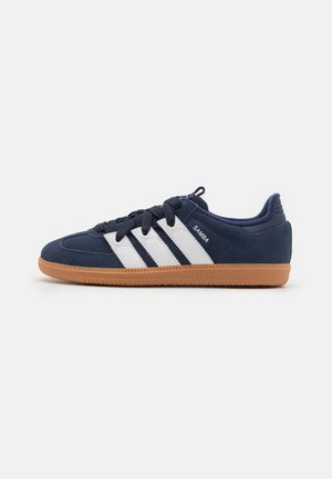Baskets Adidas Samba bleu marine avec bandes blanches, lacets noirs et semelle en gomme, vues de côté sur fond blanc.