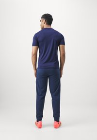 Marineblauw sportshirt met korte mouwen, gecombineerd met marineblauwe joggingbroek en felroze sneakers, met een aansluitend ontwerp en een gladde stoftextuur.