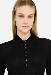 Polo a maniche lunghe nero con una texture morbida e leggera. Presenta un colletto classico e sette bottoni frontali con dettagli metallici.