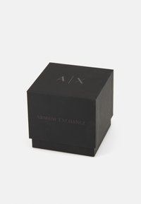 Melns kvadrātveida kastīte ar matētu apdari, kuras priekšpusē ir izspiestie uzraksti "A/X" un "ARMANI EXCHANGE". Nav citu rotājumu.