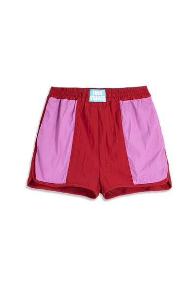 Shorts de sport rouges avec de larges panneaux latéraux violet clair et une étiquette bleue et blanche "BOBO CHOSES" sur la ceinture élastique.