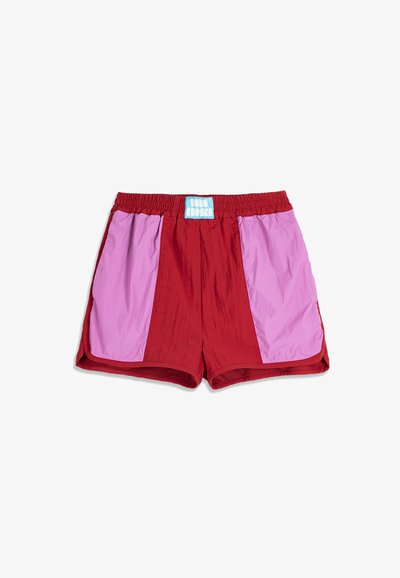 Shorts de sport rouges avec de larges panneaux latéraux violet clair et une étiquette bleue et blanche "BOBO CHOSES" sur la ceinture élastique.