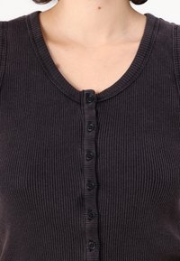 Primo piano della parte superiore del torace di una donna che indossa un top senza maniche grigio scuro a coste, con bottoni e scollo a barca.