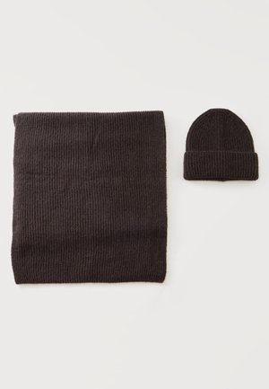 Bufanda de punto acanalado marrón oscuro y gorro plegado a juego sobre un fondo claro.
