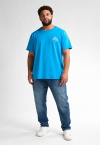 Světle modré bavlněné tričko s krátkým rukávem a kulatým výstřihem, s malou bílou grafikou na levé hrudi. V kombinaci s modrými džíny.