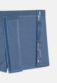 Pantalones cortos azules de tela suave con una cinturilla lisa, paneles de textura en contraste y un acento lateral decorativo con patrón.