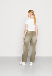 Calças largas femininas em verde oliva com uma textura desgastada, quatro bolsos e uma cintura alta, combinadas com uma t-shirt justa branca e ténis.