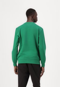Felpa verde realizzata in misto cotone, con collo rotondo, polsini e orlo a costine, e una texture liscia. Design semplice senza motivi visibili.