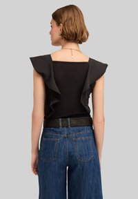 Top nero con spalle arricciate, abbinato a jeans blu a vita alta con una cintura nera texturizzata e tasche, visto da dietro.