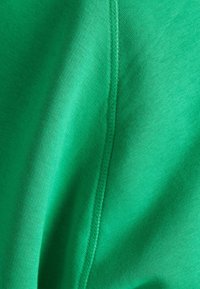 Jasně zelená tkanina s hladkým povrchem. Obsahuje viditelné švy podél švů, což vytváří čistý, strukturovaný vzhled.