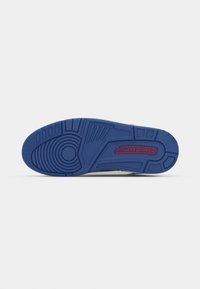 Semelle en caoutchouc bleue d'une basket avec un motif de bande de roulement circulaire et un logo rouge "JORDAN" en relief près du talon.