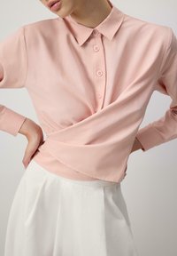 Light pink button-up shirt with a collar, wrap design, and long sleeves. Features a smooth texture and neatly sewn button placket.