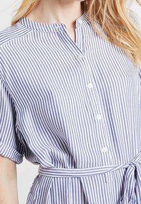 Knappligg skjorta i lätt tyg, med vertikala blå och vita ränder, en mjuk krage, korta ärmar och ett knutet midjebälte.