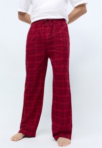 Pantalons de pyjama à carreaux rouges avec une taille élastique et un cordon de serrage, présentant une coupe ample et une texture douce. Pas de logos visibles.