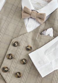 Gilet beige à carreaux avec six boutons foncés, porté avec une chemise blanche et un nœud papillon beige clair, agrémenté d'un pochettede costume à motifs.